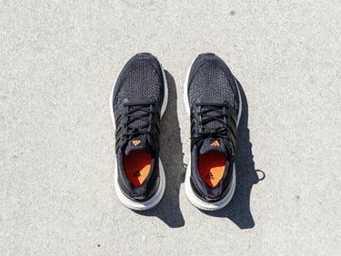 Overhead flatlay of Adidas Ultraboost running shoes on a clean concrete surface, bright daylight, minimal athletic aesthetic