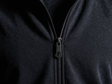 Close-up of thick, premium loopback cotton texture with a heavy-gauge steel zipper detail, high-contrast dramatic low-key lighting, deep shadows, 35mm film grain
