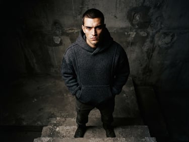 Low-angle dramatic studio shot of a model wearing a heavy-gauge charcoal structured hoodie, stoic expression, concrete textures, deep shadows, 35mm film grain