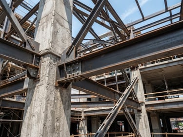 Close-up of structural steel beams and concrete columns under bright daylight, high contrast slate and steel tones, wide-angle architectural photography