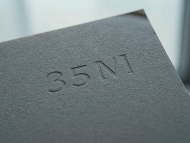 Macro close-up of premium textured gray paper stock with embossed minimalist typography, soft diffused window light, 35mm.