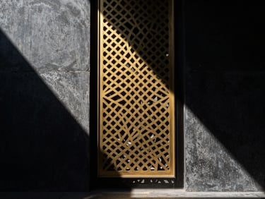 Dramatic architectural photography of a golden laser-cut metal screen casting geometric shadows on a dark concrete wall, high contrast directional sunlight, 35mm
