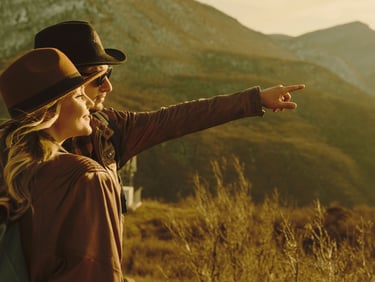 a woman in a hat and a backpack pointing at a mountain