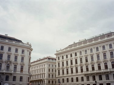 Wide environmental shot of Vienna Ringstrasse buildings under an overcast sky, muted desaturated tones, soft natural daylight, 35mm lens documentary style.