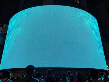 Ultra-wide low-angle shot of a massive circular LED screen glowing neon cyan, casting intense light over a packed crowd in BKC Mumbai, deep shadows