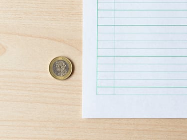 Minimalist overhead flat lay of a modern wooden workspace, a single golden coin next to a clean paper chart with green lines, soft daylight