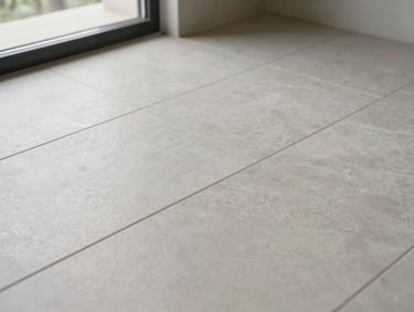 Close-up overhead shot of freshly laid ceramic floor tiles in a completed commercial interior — grout lines tight and even, natural light from side window showing material texture and finish quality