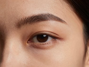 Macro photograph of the delicate under-eye area of a model, showing fine, healthy skin texture under soft, warm studio lighting.