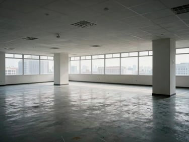 Wide interior shot of an unfurnished commercial office floor, suspended ceiling grid with recessed lighting, west-facing windows showing city rooftops, smooth screed floor, power distribution columns visible, no people, documentary framing