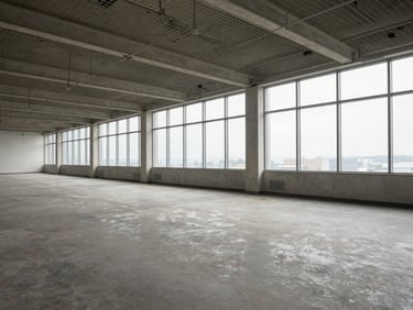 Wide interior of an empty mid-floor office suite, suspended ceiling grid, large north-facing windows with even daylight across bare screed floor, power columns at regular intervals, no furniture or people, documentary clarity