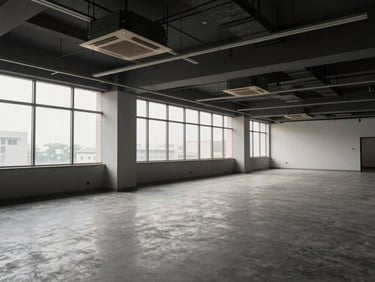 Interior wide shot of a vacant office floor in an Indian commercial building, ceiling grid and HVAC ducts visible, large windows with natural overcast daylight, power distribution columns noted, no furniture