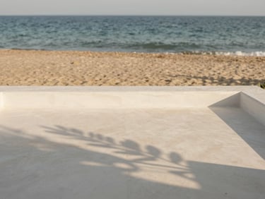 A minimalist white stone terrace overlooking the Aegean sea, soft morning light, olive branch shadow, muted sand and ocean tones, 35mm