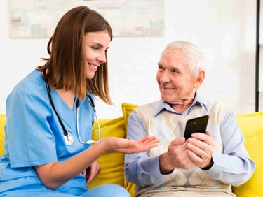 A home care worker attentively reviewing health data on a mobile phone alongside an elderly man.