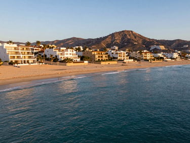 Wide-angle landscape of Palmilla beach in San Jose del Cabo, calm turquoise water of a swimmable beach, golden sand, luxury villas nestled in the hills under warm sunlight