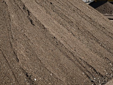 Close-up texture of compacted structural filling sand and gravel material, showing dense grading and moisture control, industrial site.