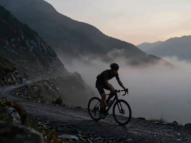 A solitary cyclist climbing a steep mountain pass at dawn, low-key dramatic lighting, cool undertones, high-contrast silhouette against mist