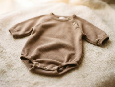 Delicate organic cotton baby romper in warm taupe, resting on a soft wool blanket, soft natural daylight, nostalgic film look