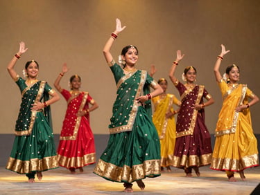 A group of young students in colorful traditional Indian dance attire performing on a stage with warm golden spotlighting, joyful expressions.