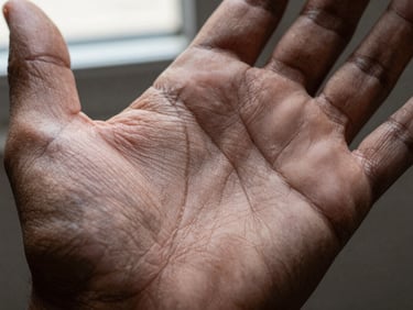 Extreme close-up of a palm center showing the head line crossing horizontally across the middle of the hand, window light from above, dark neutral background, skin tone dark brown