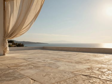 Low-angle golden hour photograph of an empty sun-drenched stone terrace overlooking the Aegean sea, linen drapes gently blowing, extreme negative space.