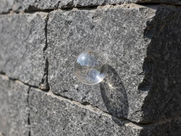 Extreme close-up of a level bubble perfectly centered on a massive slate-gray retaining wall block, showing tight stone joints and precise alignment under hard daylight.