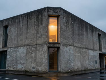 Cinematic wide shot of a rain-slicked concrete brutalist building facade at twilight, a single amber light glowing from a high window