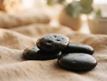Macro shot of smooth dark basalt stones resting on soft linen, warm golden-hour window light, diffused focus, serene spa setting.