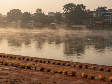Distant view of a quiet riverside ghat at sunrise, soft golden mist rising, quiet contemplative mood, 35mm lens