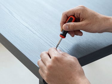 Hands of an operator using a precision screwdriver to assemble a designer wooden table, close-up, clean focus