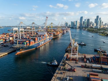 Wide environmental shot of container ships docked at PortMiami, morning daylight reflecting off deepwater hulls, crisp focus, 35mm