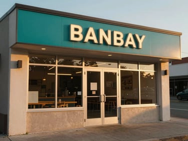 Golden-hour exterior shot of a small restaurant storefront, a freshly installed teal-toned sign above the door, warm light catching the lettering from a low angle, empty pavement in front