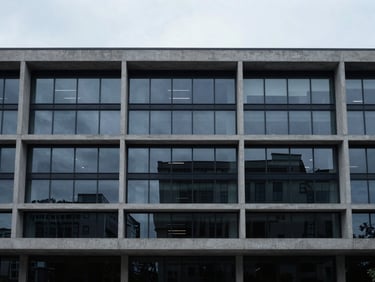 Architectural wide angle of a modern minimalist concrete and glass office facade, cool diffused daylight, desaturated navy tones.