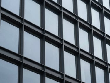 Tight abstract close-up of architectural steel and glass facade under cool overcast light, desaturated navy tones, sharp focus, 35mm lens.
