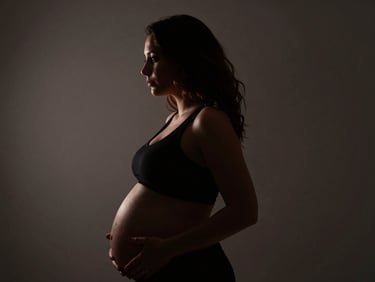 Dramatic silhouette of a pregnant woman, hard side lighting, deep chiaroscuro.