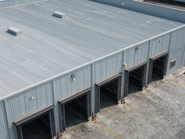 Overhead documentation-style photograph of a flex industrial building roofline and loading docks, cool midday light, concrete apron visible, no vehicles or people, utilitarian and precise