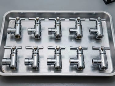 Overhead catalog shot of chrome faucet bodies lined in a factory tray, studio strobe lighting, flat even illumination, tight product detail showing polished finish and valve fittings, no warmth