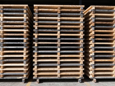 Straight-on geometric shot of neatly stacked structural timber bundles in warehouse racks, high-contrast daylight, sharp side-lighting, raw wood tones.