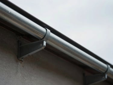 Clean, clear metal gutters running along a roofline, free of debris, under a bright overcast sky.