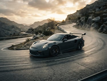 Wide panning shot of a dark grey sports car cornering hard on a remote mountain pass at golden hour