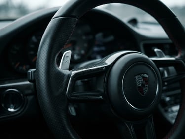 High-contrast studio detail shot of a hand-stitched leather steering wheel and machined metal paddle shifters, moody lighting