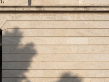 Architectural close-up of a limestone facade with clean horizontal lines, shadow from a nearby tree, soft afternoon light