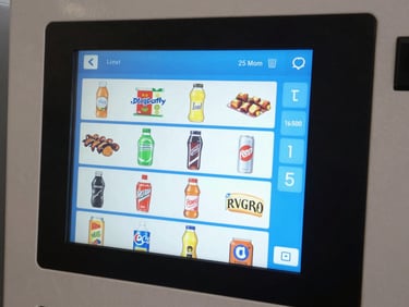 Tight close-up of a vending machine touchscreen interface displaying a product grid and live inventory indicators, bold blue UI elements visible, daylight-balanced studio lighting, no hands
