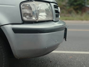 Close-up of a vehicle front bumper with minor dent on a Mexican roadside, natural daylight, authentic documentary framing