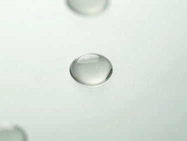 Macro close-up of transparent gel droplets on a clean glass surface, bright diffused daylight, clinical white and soft sage tones.