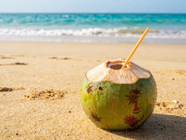 Vibrant close-up of a fresh coconut drink on a golden sand beach, bright natural sunlight, turquoise ocean background.