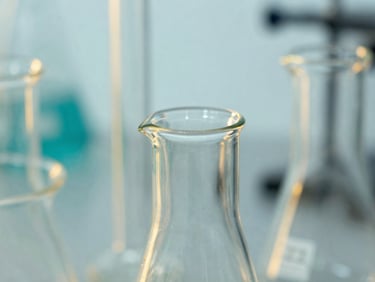 Macro close-up of high-end borosilicate laboratory glassware reflecting crisp studio light, subtle gold and teal backlighting, sharp focus, 35mm