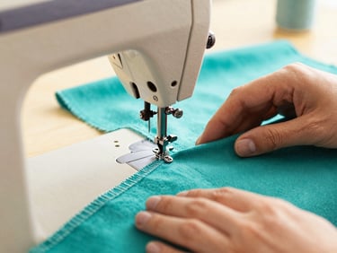 Close-up of a vintage sewing machine stitching vibrant teal fabric, thread details, hands of a craftsman, warm editorial lighting