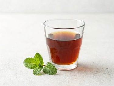 A glass of clean pour-over specialty coffee next to a small fresh mint sprig on a light stone table, bright airy lighting.