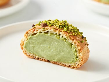 Close-up of a single choux pastry sliced in half, revealing a rich green pistachio filling, clean ceramic surface, shallow depth of field
