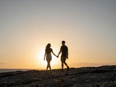 Cinematic wide shot of a couple walking hand-in-hand along a rugged coastline at sunset, warm backlighting, expansive sky, low horizon, natural motion.